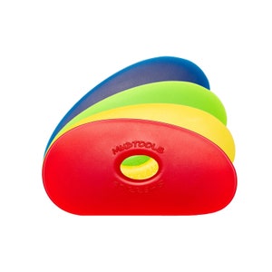 May include: A stack of colourful Mudtools Sherrill Mudtools pottery rib tools in red, yellow, green, and blue. The red rib has the brand name and product name printed on it, and a hole in the centre.