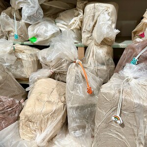 May include: A collection of white and brown clay wrapped in clear plastic bags. Some of the bags have peace sign stickers on them.