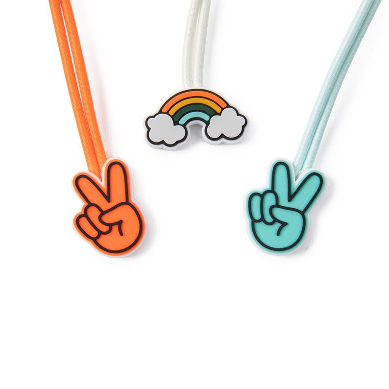 May include: Three colorful elastic hair ties with peace sign and rainbow charms. The hair ties are orange, blue, and white.