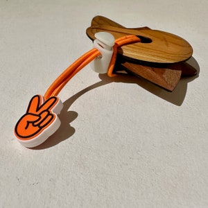 May include: Orange and white peace sign shaped rubber toggle with a wooden ring attached to a long orange elastic cord.