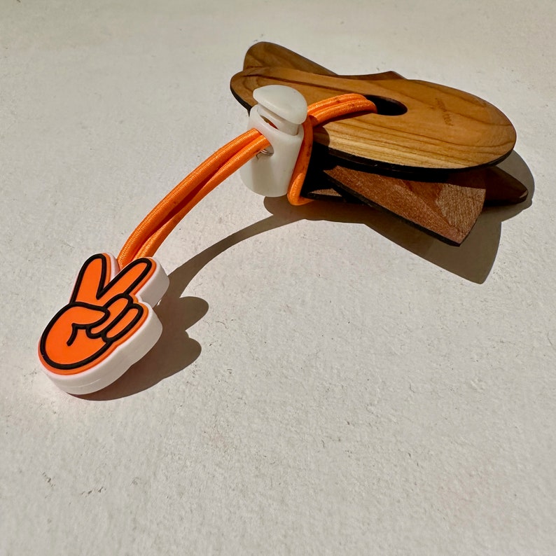 May include: Orange and white peace sign shaped rubber toggle with a wooden ring attached to a long orange elastic cord.