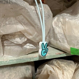 May include: A stack of white plastic bags with a blue peace sign charm attached to the top bag.