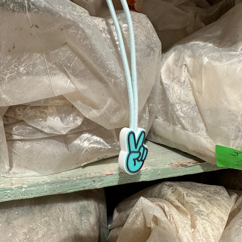 May include: A stack of white plastic bags with a blue peace sign charm attached to the top bag.