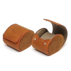 May include: Two brown leather watch boxes, one open and one closed. The open box has a soft gray interior.