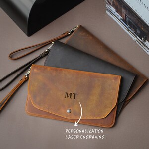 May include: Three leather wallets in brown, black, and tan. The tan wallet has the initials "MIT" engraved on the front. The wallets have a flap closure and a wrist strap.