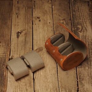 May include: A brown leather case with two gray felt inserts for storing small items. The case is open and the inserts are visible. The case is sitting on a wooden surface.