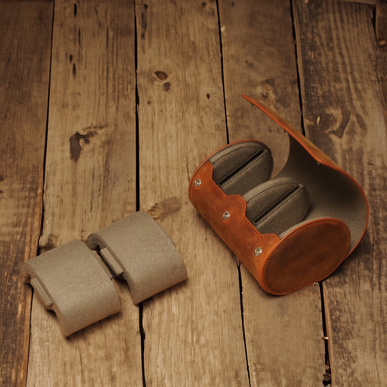 May include: A brown leather case with two gray felt inserts for storing small items. The case is open and the inserts are visible. The case is sitting on a wooden surface.