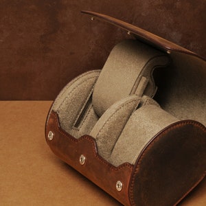 May include: A brown leather watch box with four compartments for storing watches. The box has a hinged lid and is lined with soft, beige fabric.
