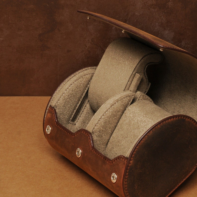 May include: A brown leather watch box with four compartments for storing watches. The box has a hinged lid and is lined with soft, beige fabric.