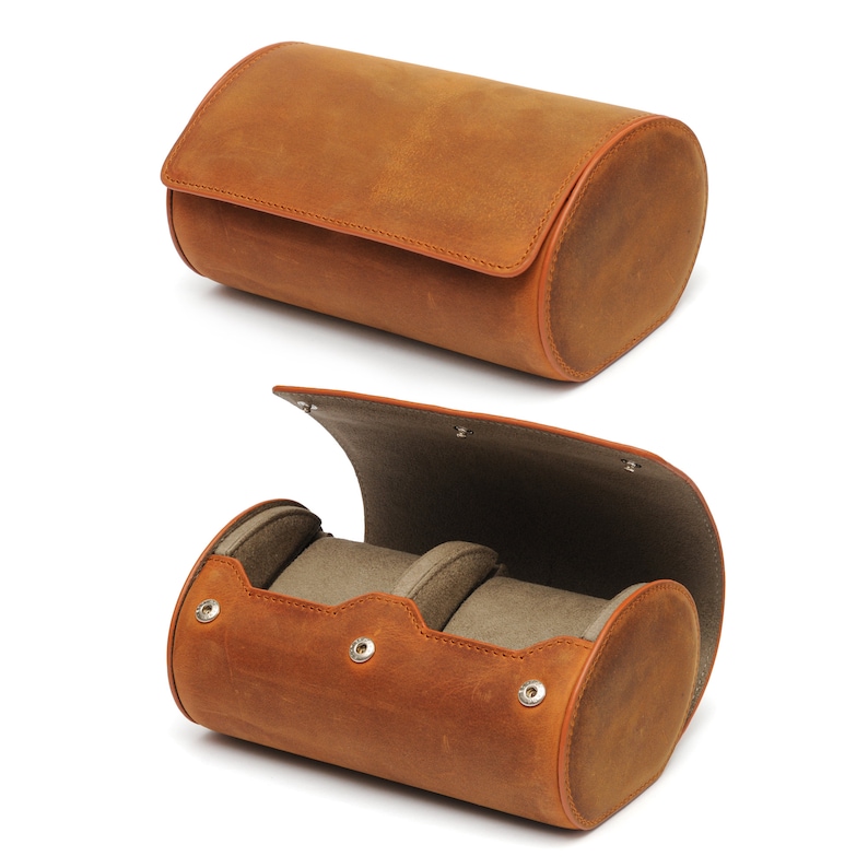 May include: A brown leather watch roll with two compartments for storing watches. The roll is open to reveal the soft, gray interior lining.