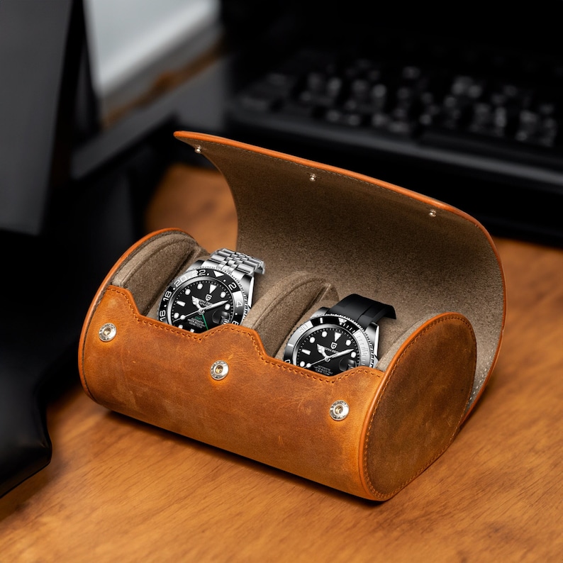May include: A brown leather watch roll with two watches inside. The watches have black faces and silver bands.