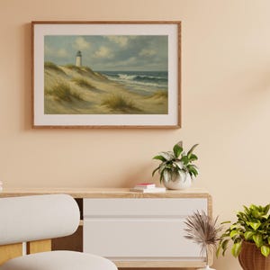 May include: A framed landscape painting of a coastal scene. The artwork depicts a white lighthouse atop a sandy dune, with ocean waves crashing on the shore under a cloudy sky. The frame is made of wood.