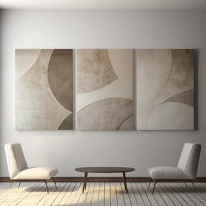 Könnte beinhalten: Drei abstrakte Wandkunst-Paneele in Beige- und Cremetönen. Das Kunstwerk zeigt überlappende kreisförmige Formen mit strukturierten Oberflächen. Darunter vervollständigen zwei weiße Stühle und ein dunkelbrauner Tisch das moderne Innendesign.