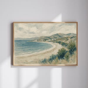 May include: A framed landscape painting depicts a coastal scene. The artwork features a sandy beach, turquoise water, and rolling green hills under a cloudy sky. Small white buildings dot the shoreline. The painting is in a wooden frame.