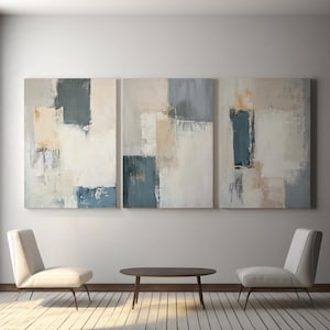 May include: Three abstract paintings with a modern design. Each canvas features a mix of rectangular shapes in shades of white, beige, and blue-gray. The paintings are displayed above two white chairs and a dark brown table.