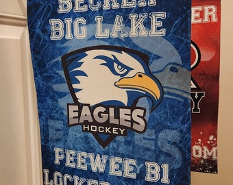 Puede incluir: Señal de vestuario de hockey azul y blanca con el texto "Becker Big Lake Eagles Hockey Peewee B1 Locker Room". La señal presenta un gráfico de águila azul y amarilla.