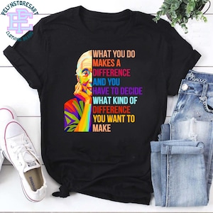 Puede incluir: Camiseta negra con un retrato pop art colorido y el texto "WHAT YOU DO MAKES A DIFFERENCE AND YOU HAVE TO DECIDE WHAT KIND OF DIFFERENCE YOU WANT TO MAKE." La camiseta se muestra con vaqueros azules y zapatillas blancas.