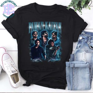 May include: Black t-shirt featuring a graphic of multiple people with the text "PAWAN KALYAN" in a blue, glowing font. The design is a portrait-style image. The shirt is paired with blue jeans and white sneakers.