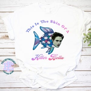 May include: White t-shirt with a blue and purple fish with a human face. The text "This is the skin of a Killer Bella" is printed on the shirt.