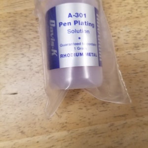 May include: A clear plastic bottle with a blue label that reads "A-301 Pen Plating Solution Guaranteed to contain 1 Gram RHODIUM METAL Davis-K".