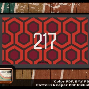 Puede incluir: Un patrón de punto de cruz con un diseño geométrico rojo y naranja con el número 217 en blanco. El patrón está enmarcado en un marco negro con un fondo de madera.