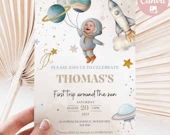 May include: A blue and gold space-themed first birthday party invitation with a photo of a baby dressed as an astronaut. The invitation says "Please join us to celebrate Thomas's First Trip Around The Sun" and includes the date, time, and location of the party.