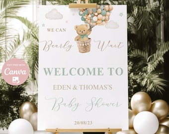 May include: A baby shower welcome sign on an easel. The sign features a teddy bear in a hot air balloon with the text "We Can Bearly Wait" and "Welcome to Eden & Thomas's Baby Shower". The date 20/08/23 is also displayed. The sign is surrounded by balloons.