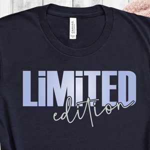 Op de afbeelding: Een marineblauw t-shirt met de tekst "LIMITED edition" in een lichtblauwe gradiënt. De tekst is in een vet, blokkerig lettertype met een handschrift voor "edition".