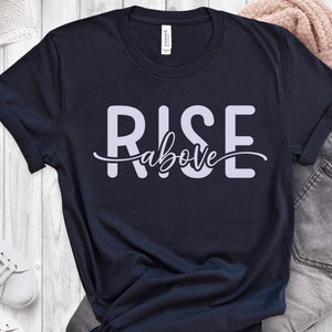 Könnte beinhalten: Ein marineblaues T-Shirt mit dem Aufdruck "RISE above" in helllila.