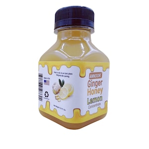 May include: A clear plastic bottle of lemon ginger honey concentrate. The bottle is labeled with the brand name "ANNOOR" and the product name "Ginger Honey Lemon Concentrate". The label also includes a small image of a lemon and ginger root.