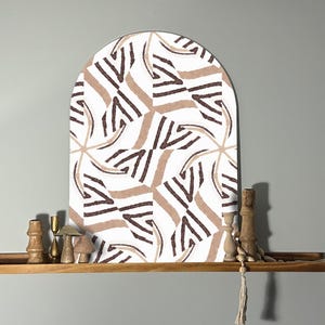 May include: A white arch-shaped wall decor with a geometric pattern in brown and beige. The decor is on a wooden shelf with decorative items.