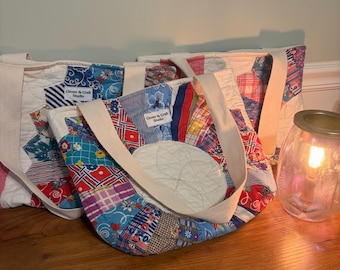 May include: Two quilted tote bags made from colorful patchwork fabric featuring various floral, striped, and geometric patterns. Each bag has cream-colored fabric handles and a white label reading Clover & Craft Studio stitched on the front.