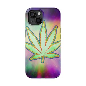 Può includere: Una custodia per smartphone con una grafica centrale raffigurante una foglia di cannabis verde chiaro, delineata con colori arcobaleno. Lo sfondo presenta un motivo a nebulosa cosmica con sfumature di viola, rosa, giallo e blu.