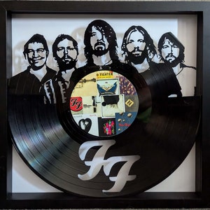 May include: A framed black vinyl record with a white "FF" logo. The record is partially obscured by a silhouette of five people, possibly a band.