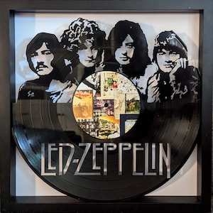 May include: A black vinyl record with a silver silhouette of the band Led Zeppelin. The silhouette shows the four band members, with a collage of album covers behind them.
