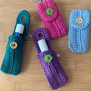 May include: Four crocheted keychain holders with different colored yarn and buttons. The holders are designed to hold lip balm or other small items.