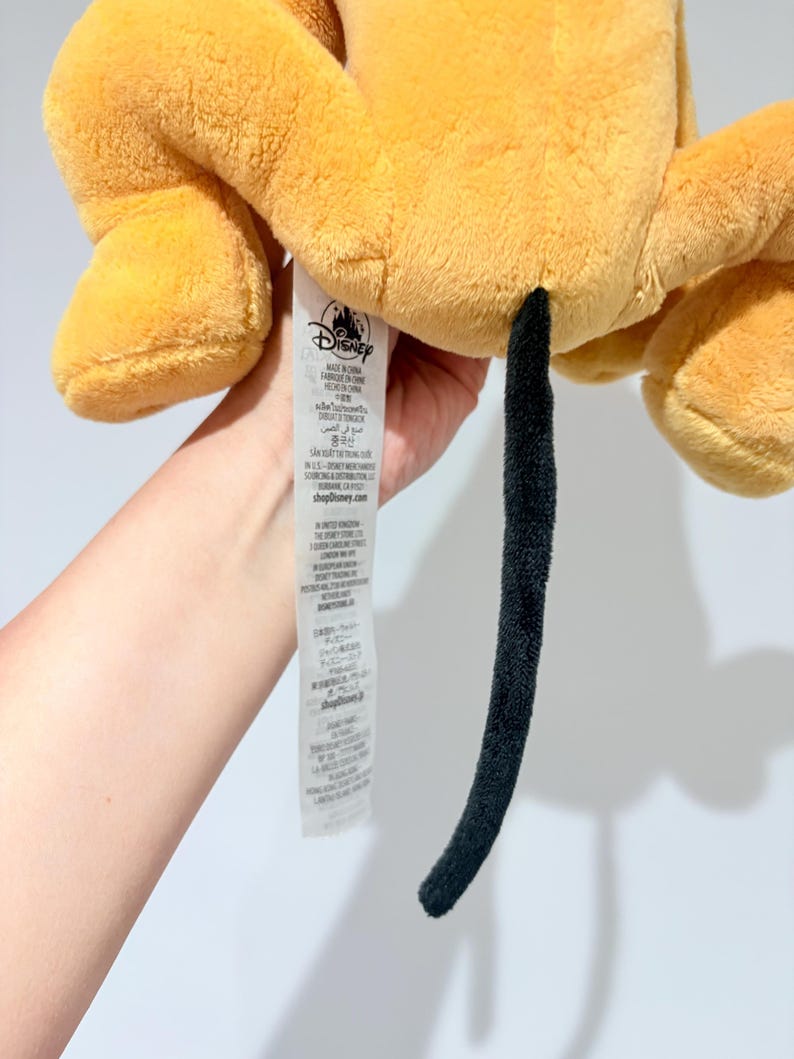 May include: A plush toy in shades of yellow and orange, featuring a long, black tail. The toy has a tag with the Disney logo. The plush appears soft and cuddly, with visible stitching details.