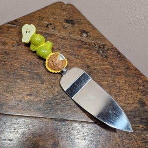 May include: A silver cake server with a green pear and a pie slice handle. The handle is made of ceramic and the blade is stainless steel.