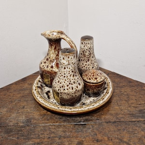 May include: A brown and white speckled ceramic salt and pepper shaker set with a matching creamer and a small dish. The set is on a brown wooden surface.