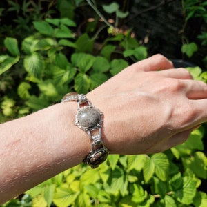 May include: A silver bracelet with a chain link design and three round, grey and brown gemstone accents.