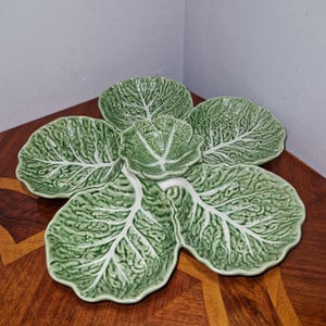 May include: A green ceramic cabbage leaf serving dish with five individual bowls. The dish is designed to look like a cabbage with realistic details.