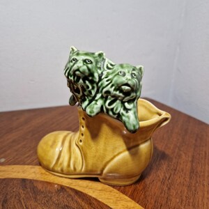 May include: A ceramic boot planter with two green ceramic cats on top. The boot is brown and has a white button detail.