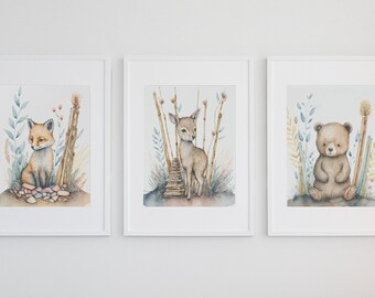 May include: Three framed watercolour illustrations of woodland animals. The first shows a fox sitting on a pile of rocks with tall grass and flowers behind it. The second shows a fawn standing on a wooden bridge with tall grass and flowers behind it. The third shows a bear sitting on a rock with tall grass and flowers behind it.