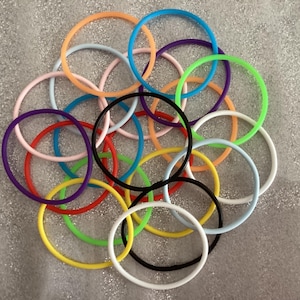 May include: A collection of colorful silicone rings in various shades of blue, green, yellow, orange, red, pink, and purple. The rings are arranged in a circular pattern, with a black ring in the center.