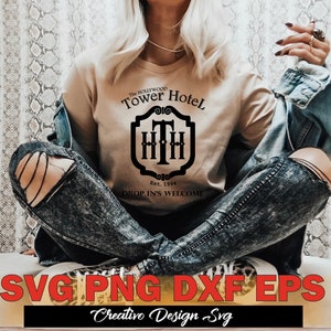 May include: A beige t-shirt with a black graphic design featuring the text "The Hollywood Tower Hotel" and a crest with the letters "THH" inside. The text "Est. 1994" and "Drop In's Welcome" are also included in the design.