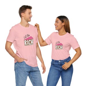 May include: Two people wearing matching pink t-shirts with the text "Eat the Rich" and a graphic of a cake. The shirts are short-sleeved and the models are wearing blue jeans. The background is white.