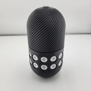 May include: A black, cylindrical object with a textured, spiral design on the top portion. The bottom section features a series of white, cross-shaped accents. The object is set against a plain white background.