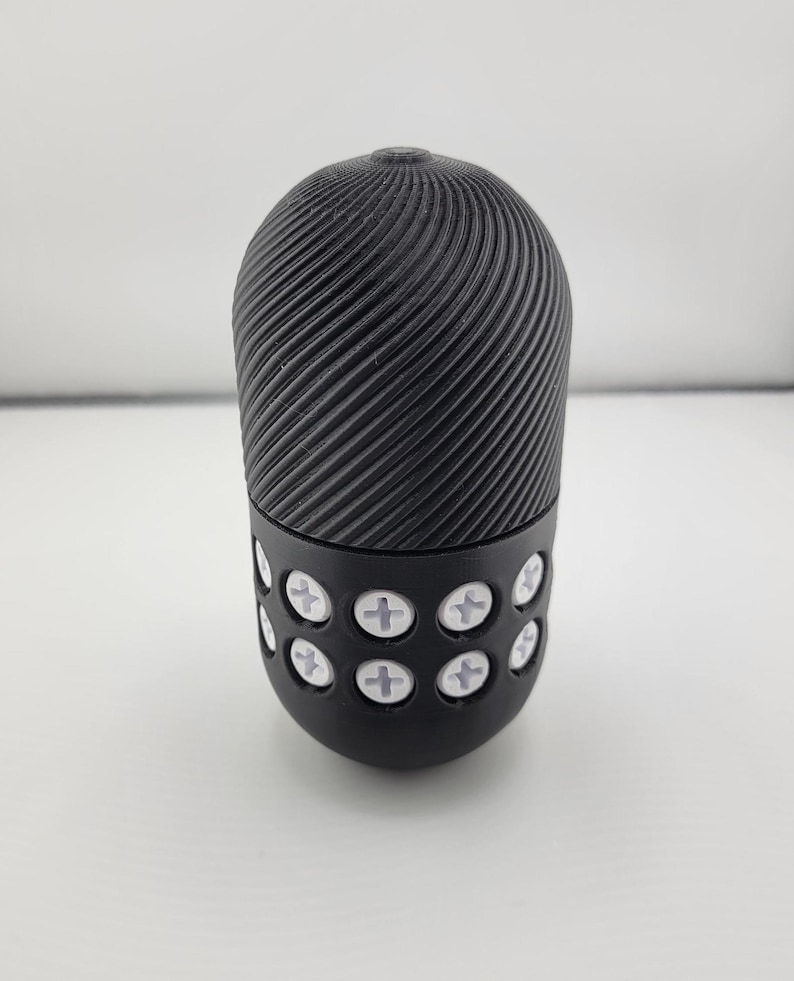 May include: A black, cylindrical object with a textured, spiral design on the top portion. The bottom section features a series of white, cross-shaped accents. The object is set against a plain white background.
