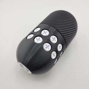 May include: A black, oval-shaped object with a textured, ridged top and a series of white, cross-shaped accents. The object has a smooth, rounded base and appears to be made of a solid material.