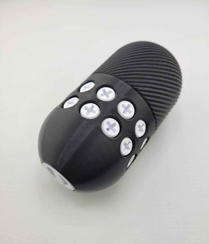 May include: A black, oval-shaped object with a textured, ridged top and a series of white, cross-shaped accents. The object has a smooth, rounded base and appears to be made of a solid material.